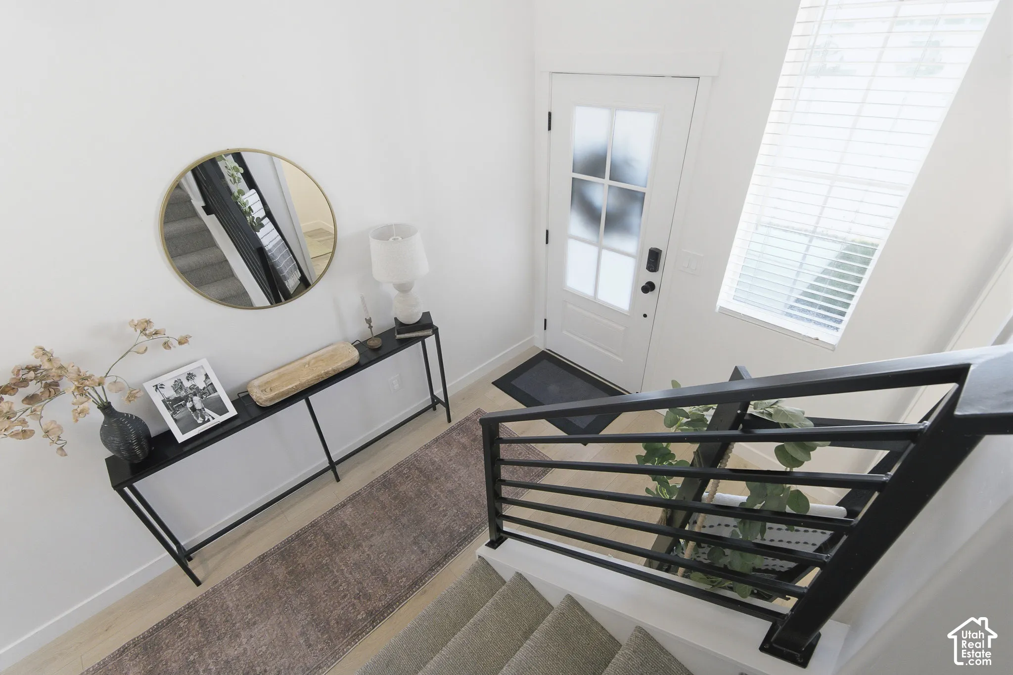 Entryway featuring high ceilings, tall windows with horizontal blinds, light-toned wood-finish flooring, and a staircase with a black metal horizontal-bar railing