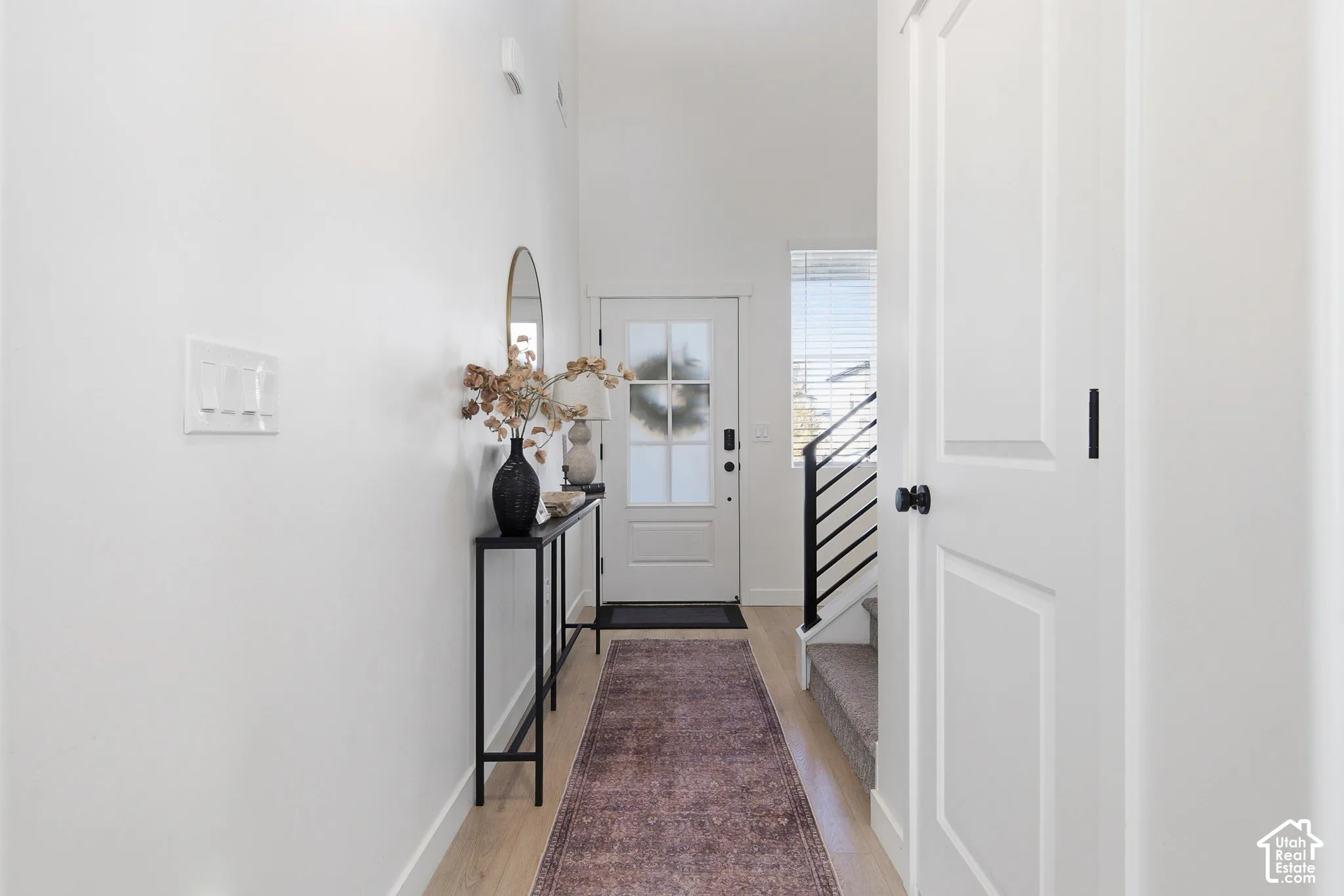 Entryway featuring vaulted ceilings, light-toned wood-finish flooring, a multi-pane glass entry door, and a staircase with a matte black railing