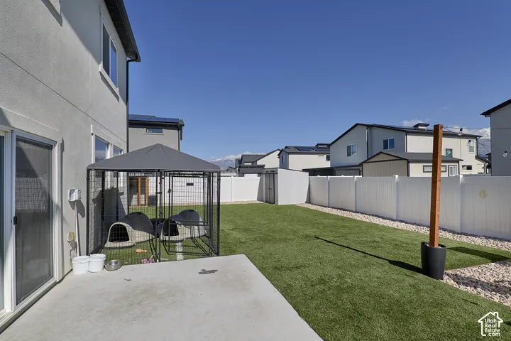 Fenced-in backyard featuring a concrete patio, synthetic turf lawn, gravel perimeter, and a detached storage shed