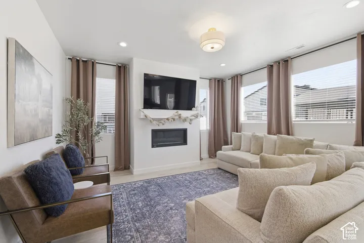Living area featuring a modern linear fireplace, recessed lighting, neutral walls, wood-finish flooring, and multiple large windows