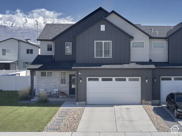 Modern two-story exterior featuring vertical board-and-batten siding, light stone veneer masonry, a multi-gabled roofline, an attached two-car garage, and mountain scenery