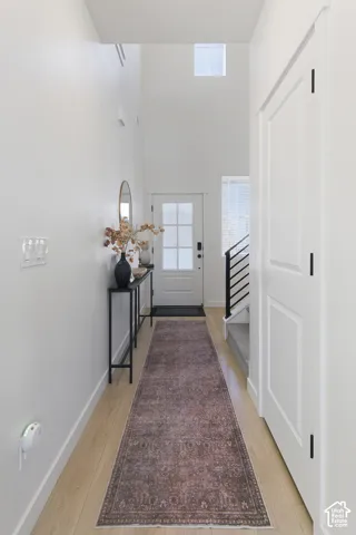 Foyer featuring high ceilings, light-tone wood-finish flooring, a multi-pane glass-panel entry door, and a staircase with a modern metal railing