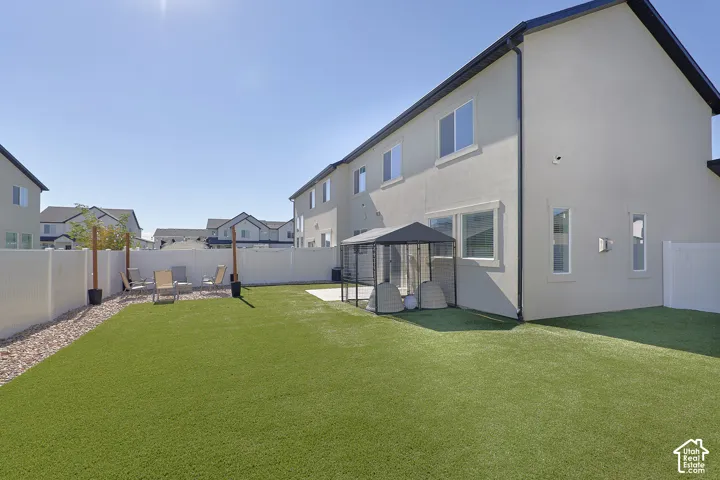 Backyard featuring synthetic turf, concrete patio, white vinyl perimeter fencing, and a graveled area