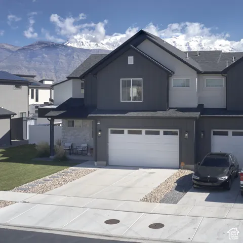 Two-story exterior featuring vertical dark siding, stone veneer accents, an attached two-car garage, and snow-capped mountain backdrop