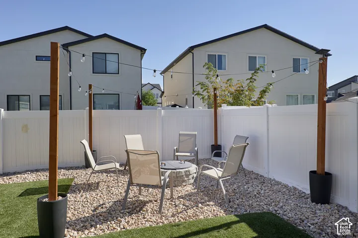 Private outdoor space featuring a stone fire pit, low-maintenance gravel ground cover, artificial turf, perimeter white vinyl fencing, and vertical support posts with string lighting