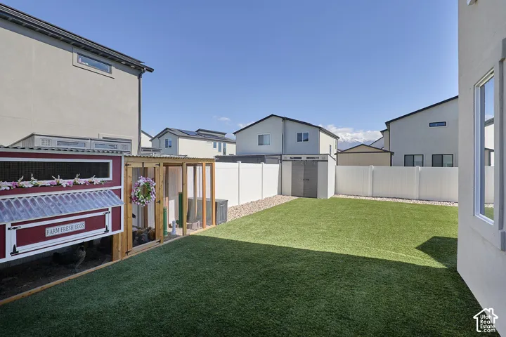 Backyard featuring synthetic turf, white vinyl privacy fencing, gravel perimeter, and a detached storage structure