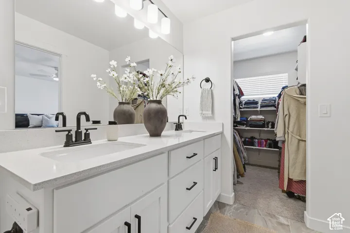 Dual-sink vanity with a quartz countertop, matte black fixtures, white cabinetry, and a full-width mirror