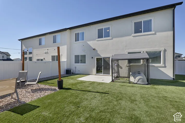 Fenced backyard featuring synthetic turf, concrete patio, and stone ground cover