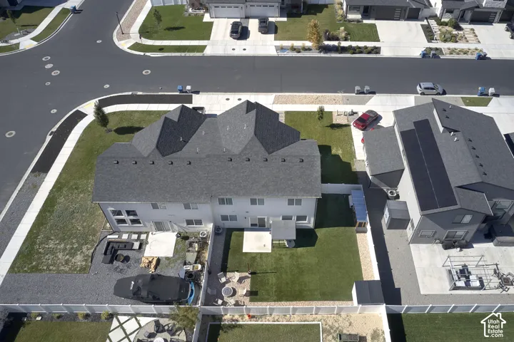 Corner lot residential property featuring a multi-pitched roofline, fenced rear yard, concrete patio, and synthetic turf lawn