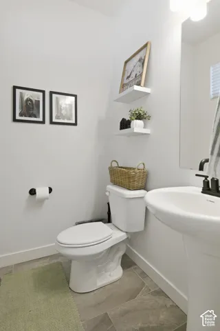 Powder room featuring a pedestal sink, matte black faucet, large-format tile flooring, wall-mounted shelving, and a vanity mirror with overhead lighting