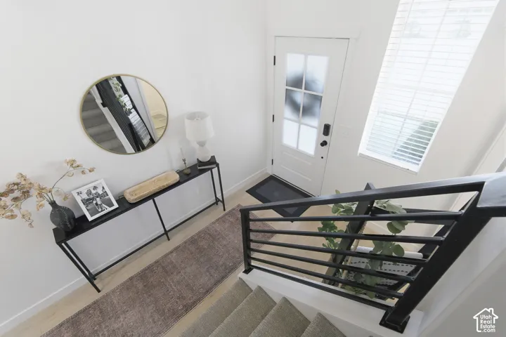 Entryway featuring high ceilings, tall windows with horizontal blinds, light-toned wood-finish flooring, and a staircase with a black metal horizontal-bar railing
