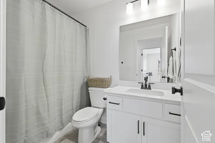 Bathroom featuring a white shaker-style vanity with stone-surface countertop, rectangular undermount sink, matte black hardware, and an expansive frameless mirror with three-bulb vanity lighting