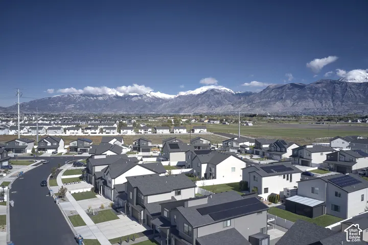Aerial perspective featuring residential lots with roof-mounted solar panels, concrete driveways, and expansive mountain range backdrop