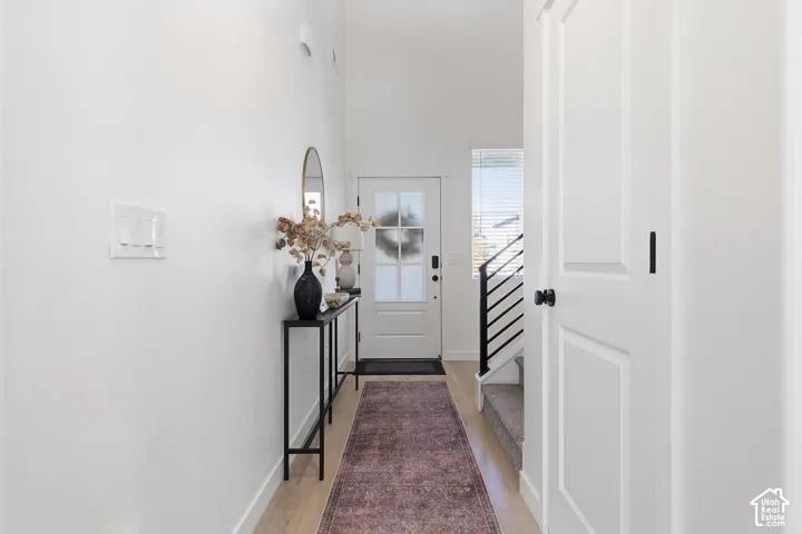 Entryway featuring vaulted ceilings, light-toned wood-finish flooring, a multi-pane glass entry door, and a staircase with a matte black railing