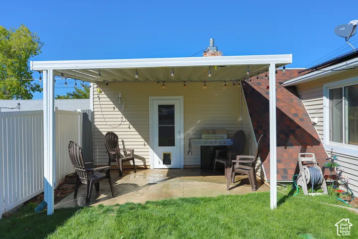 Covered concrete patio featuring a white metal pergola and a white vinyl privacy fence
