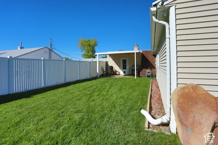 Rear exterior featuring a covered patio, vinyl privacy fencing, landscaped lawn, and brick chimney detail