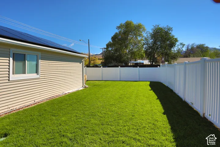 Backyard featuring a manicured lawn, white vinyl fencing, and roof-mounted solar panels