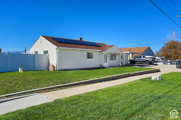 Single-story residence featuring vinyl siding, roof-mounted solar panels, concrete driveway, attached carport, and perimeter vinyl fencing