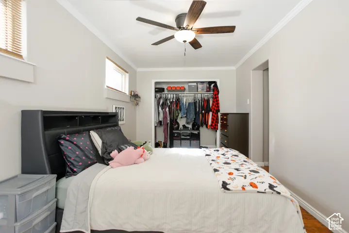 Neutral-toned room featuring wood-finish flooring, a ceiling fan with integrated lighting, crown molding, and a built-in closet