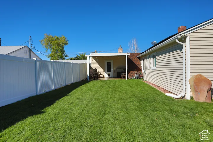 Backyard featuring a manicured lawn, white vinyl fencing, and a covered patio