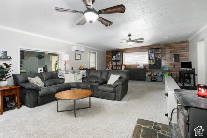 Living space featuring wood-plank wall detailing, dual ceiling fans, a wall-mounted climate control unit, and a stone hearth platform
