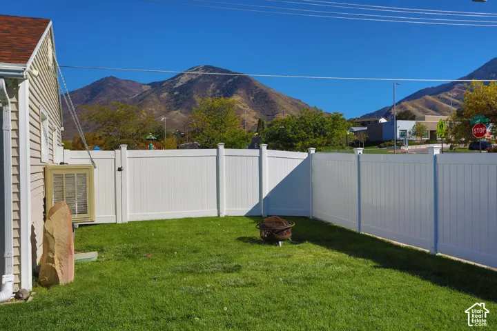 Fenced backyard featuring a manicured lawn, vinyl privacy fencing, and mountain scenery