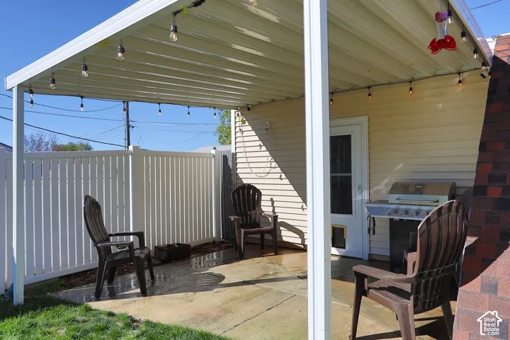 Covered patio featuring a metal awning, concrete slab flooring, and white vinyl perimeter fencing
