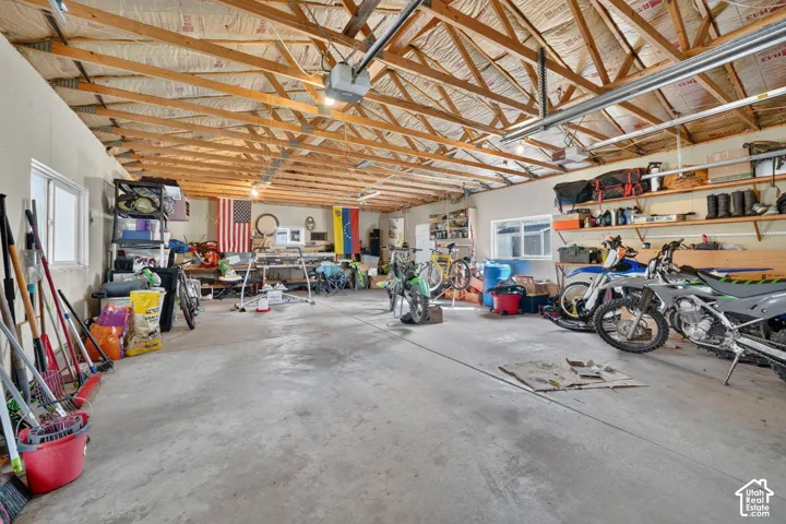 Expansive garage featuring exposed timber truss ceiling, concrete flooring, dual sliding windows, and wall-mounted shelving