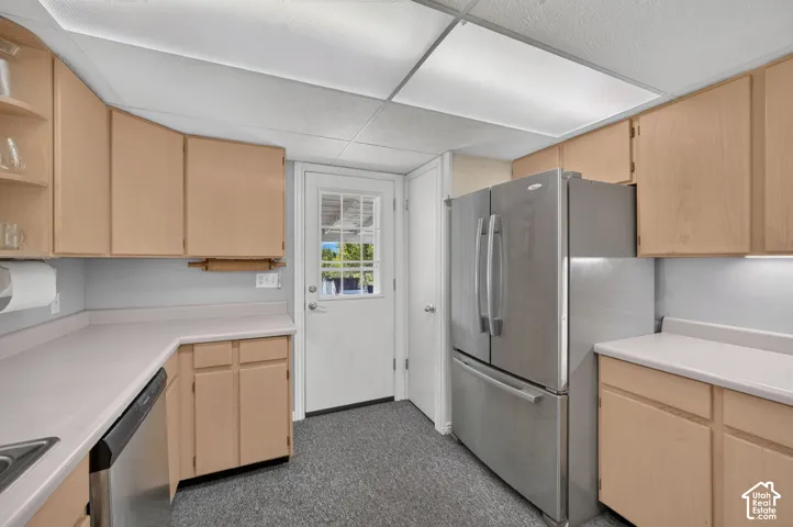 Kitchen featuring light-finish cabinetry, neutral solid-surface countertops, stainless steel refrigerator, stainless steel dishwasher, and a glass-paneled exterior door