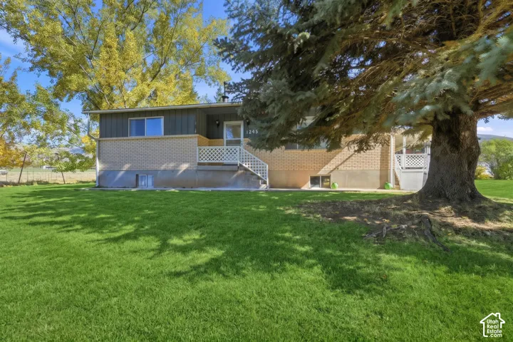 Exterior facade featuring brick masonry and vertical siding, complemented by a covered porch with lattice railings and a mature conifer tree situated on the lawn