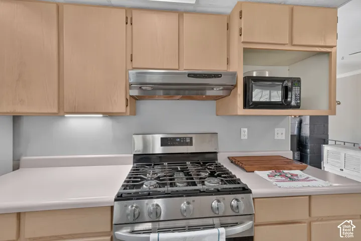 Kitchen featuring light-finish cabinetry, stainless steel gas range, stainless steel range hood, and solid-surface countertops