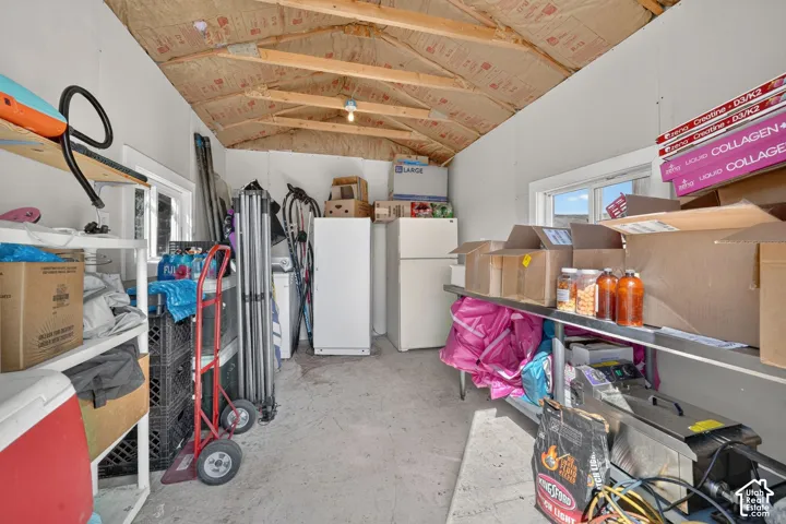 Outbuilding featuring exposed wooden roof trusses, concrete flooring, dual windows, and built-in metal shelving