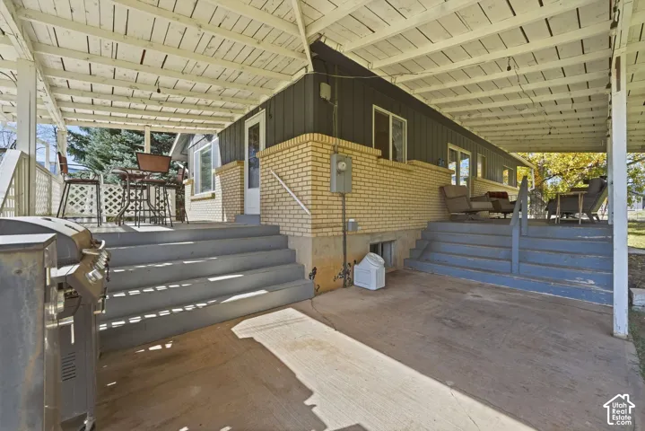 Covered patio space featuring a concrete slab surface, raised painted wood-finish stairs, horizontal board-and-batten siding, and exterior brick masonry