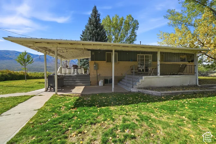 Exterior featuring an expansive covered patio, elevated wooden decking, brick and vertical siding facade, concrete walkways, and mountain backdrop