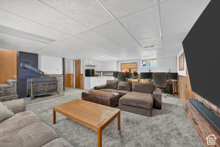 Finished lower level featuring a wood-burning stove with masonry hearth, built-in cabinetry, wood-paneled walls, and carpeted flooring