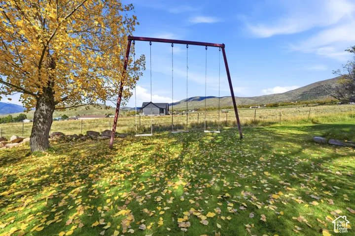 Expansive grounds featuring a mature deciduous tree, a metal swing set, and mountain scenery