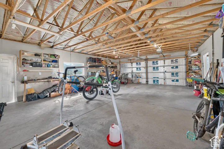 Spacious garage featuring a concrete floor, exposed truss ceiling, built-in wall shelving, and insulated overhead garage doors