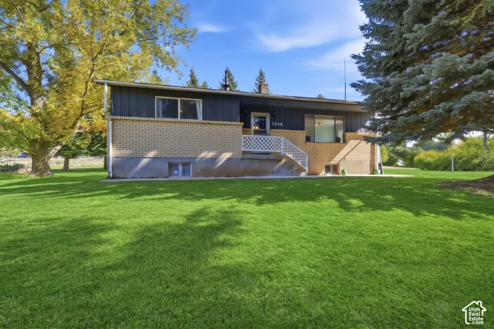 Exterior featuring a brick and dark-toned siding facade, white lattice-style stair railing, and a sprawling lawn accented by mature trees