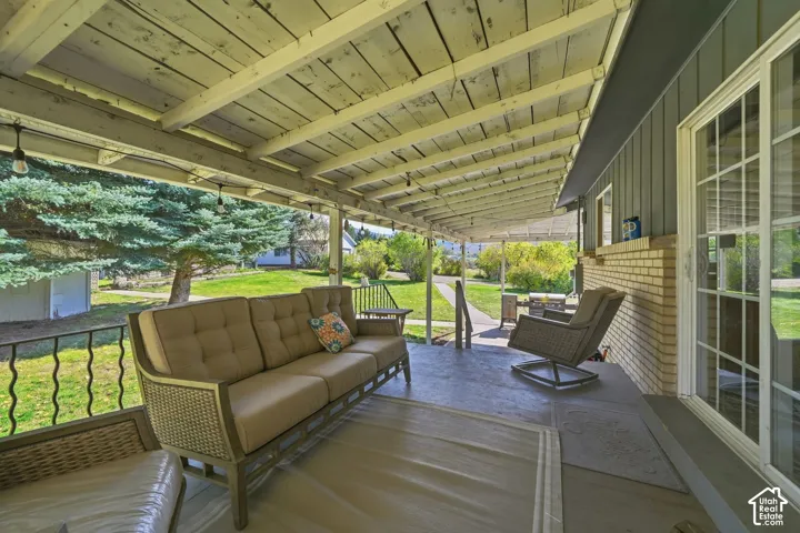 Covered patio featuring an exposed-beam ceiling, concrete flooring, decorative metal railing, and brick exterior wall siding