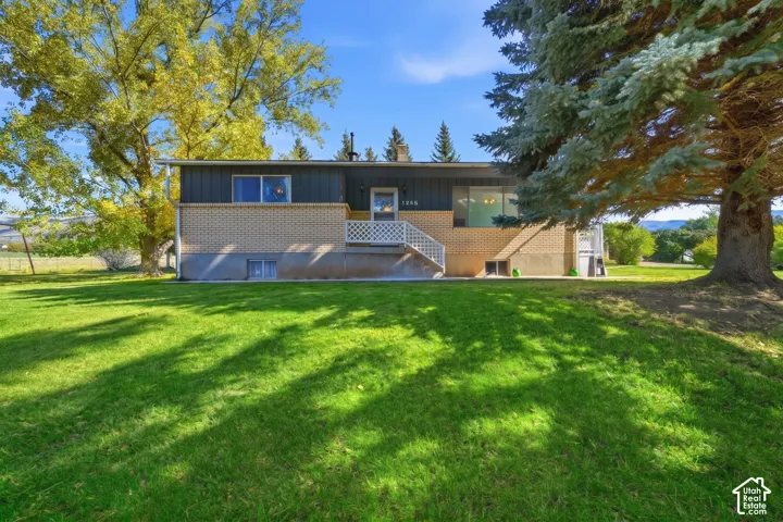 Exterior facade featuring brick masonry and horizontal paneling, an elevated entryway with a lattice-style railing, and an expansive lawn with mature trees