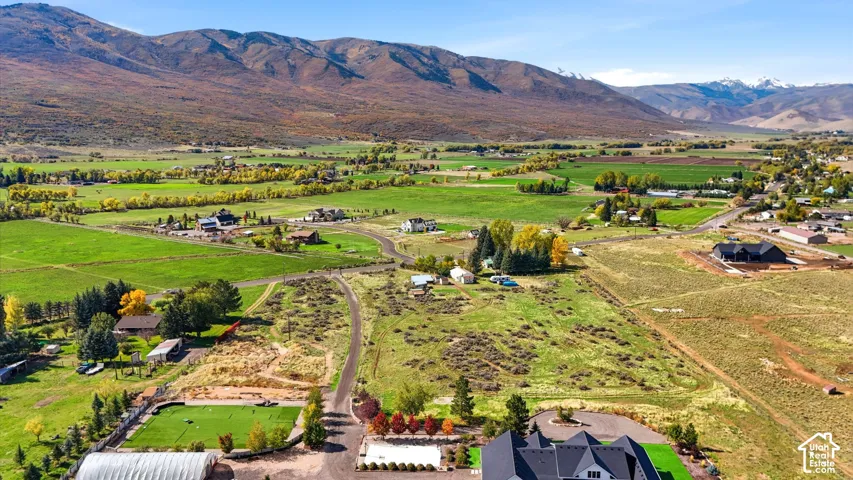Aerial perspective of expansive acreage featuring mountain backdrop, sprawling valley terrain, paved driveway, and established tree clusters