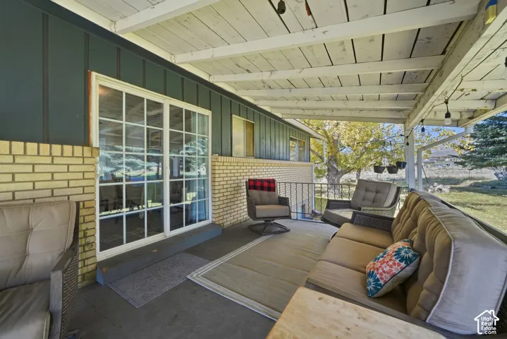Covered patio featuring a concrete floor, painted wood-beam ceiling, multi-pane sliding glass doors, and a combination of brick and vertical siding exterior walls