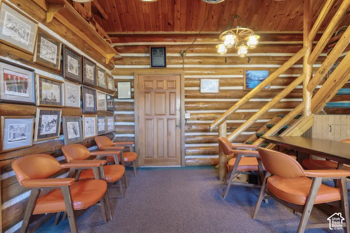 Rustic log walls with chinking, wood-paneled ceiling, wagon wheel-style chandelier, and wooden staircase with log handrail