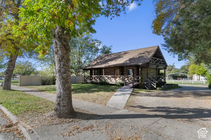 Log-construction exterior featuring a wrap-around porch with wooden lattice railing, asphalt shingle roof, and detached metal-frame carport