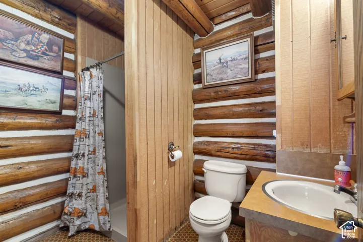 Natural log walls, vertical wood paneling, wood-beam ceiling, integrated sink vanity, and enclosed shower stall