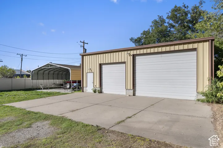 Detached metal workshop with dual garage doors, concrete apron, and separate covered carport structure