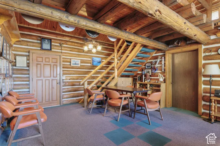 Log-cabin interior featuring exposed timber ceiling beams, horizontal log walls, and a hand-hewn wood staircase with a matching railing