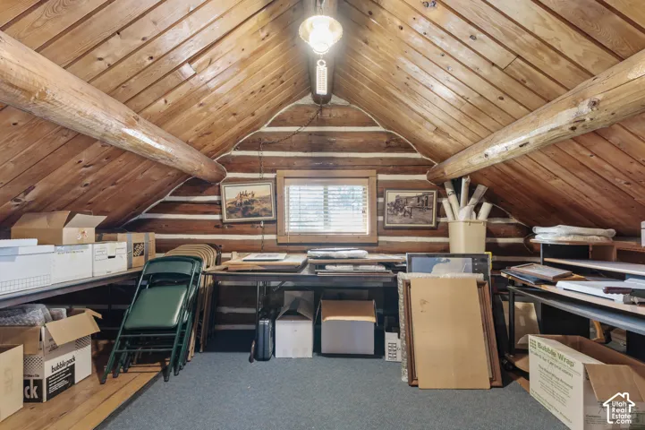 Rustic attic space featuring exposed log walls, timber rafters, a vaulted tongue-and-groove ceiling, and a central window