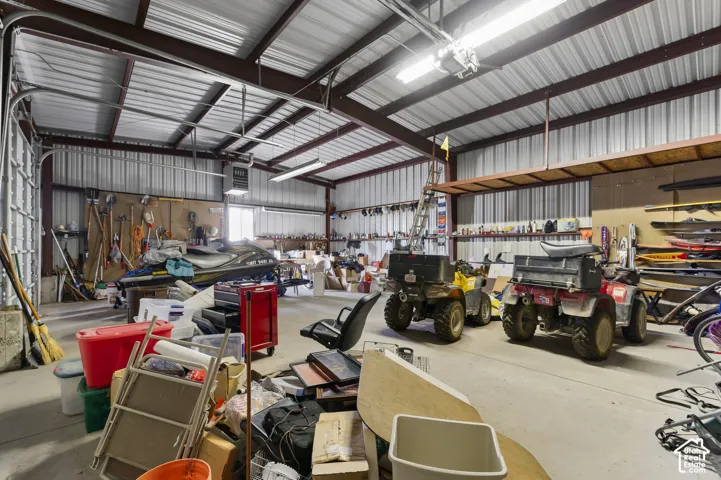 Expansive workshop featuring high vaulted ceilings, exposed steel framing, concrete flooring, and built-in perimeter shelving