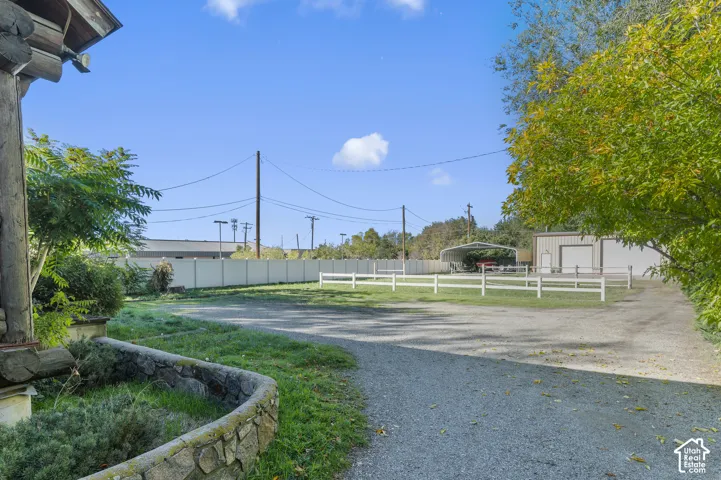 Expansive gravel lot featuring a stone-clad planter, perimeter privacy fencing, multi-rail split fencing, and a detached metal-sided structure